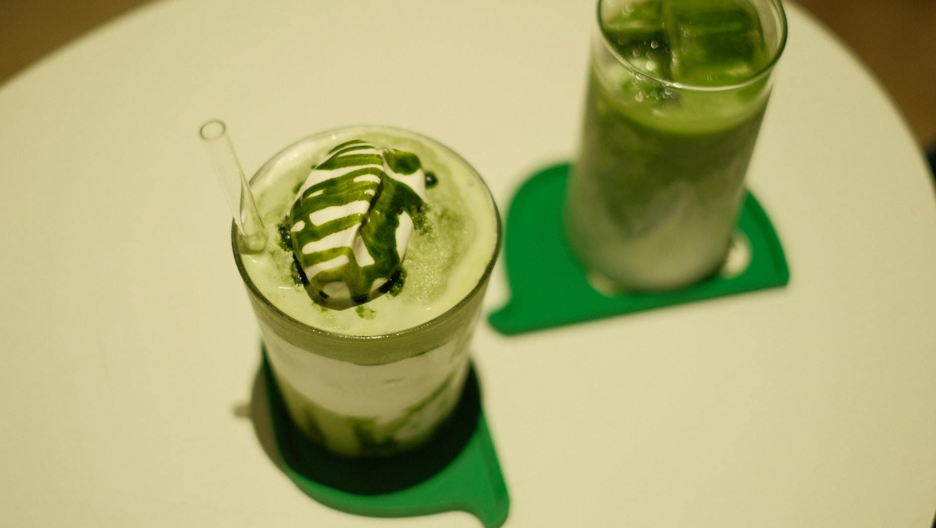 Dwa mrożone latte matcha z bitą śmietaną i polewą na stoliku