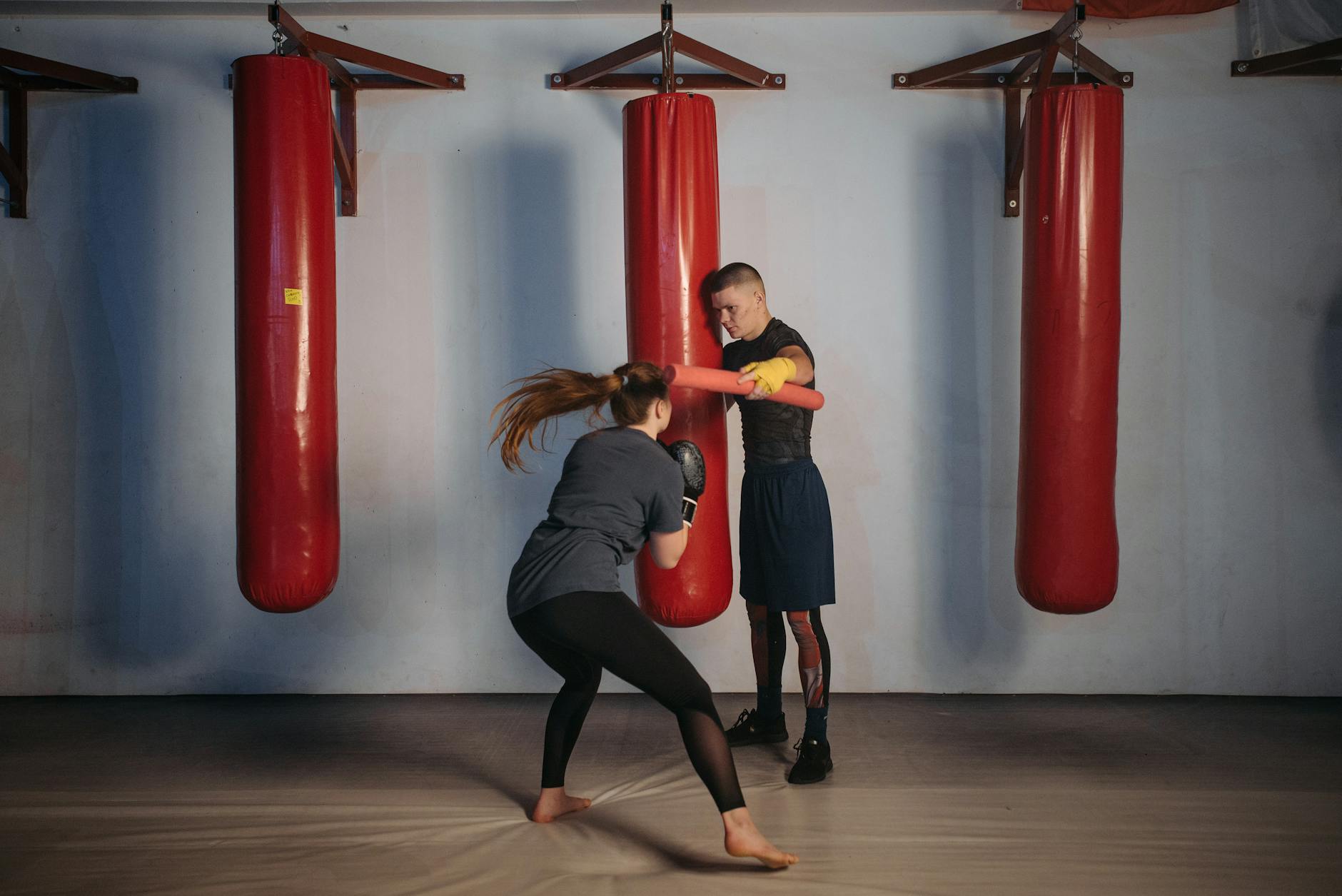 Kobieta trenuje boks z trenerem na czerwonych workach w siłowni