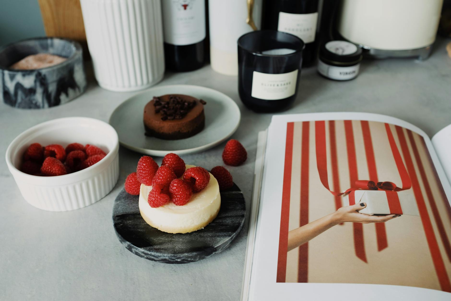 Mini serniczki na zimno w szklankach jako elegancka przekąska do kawy Serniczek z malinami na marmurowym talerzu obok czekoladowego deseru