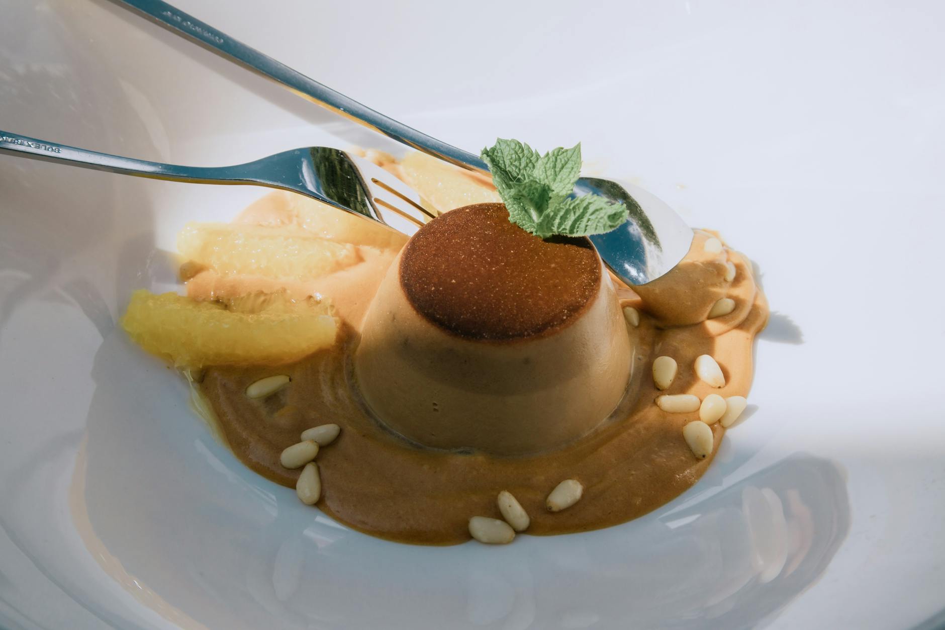 Deser panna cotta z miętą, orzeszkami piniowymi i cytrusami na talerzu