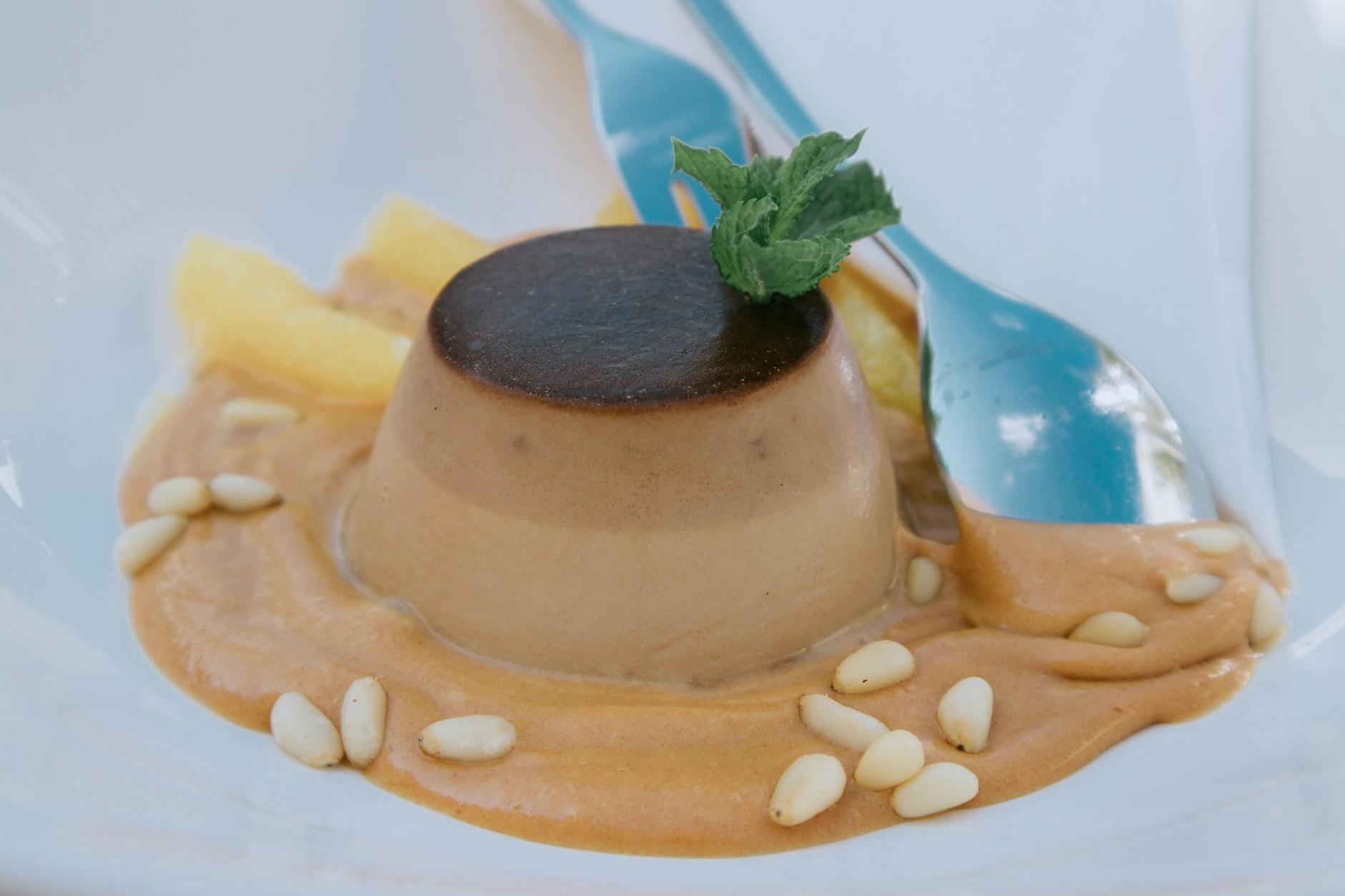 Kremowa karmelowa panna cotta z miętą z bliska, obok leży łyżeczka