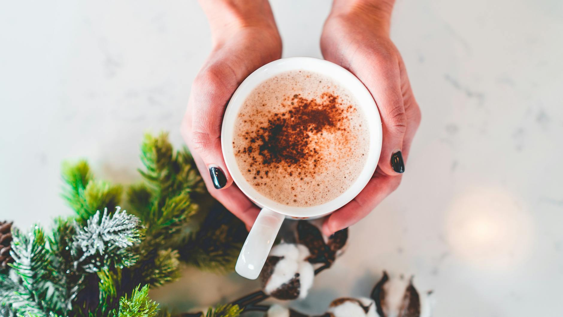 Dłonie trzymające cappuccino z cynamonem wśród zimowej zieleni