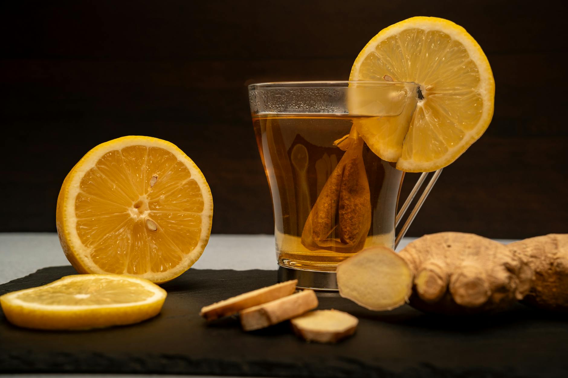 Musująca herbata imbirowa z fermentu: idealna baza do koktajli bez alkoholu Filiżanka herbaty imbirowo-cytrynowej otoczona świeżym imbirem i cytryną