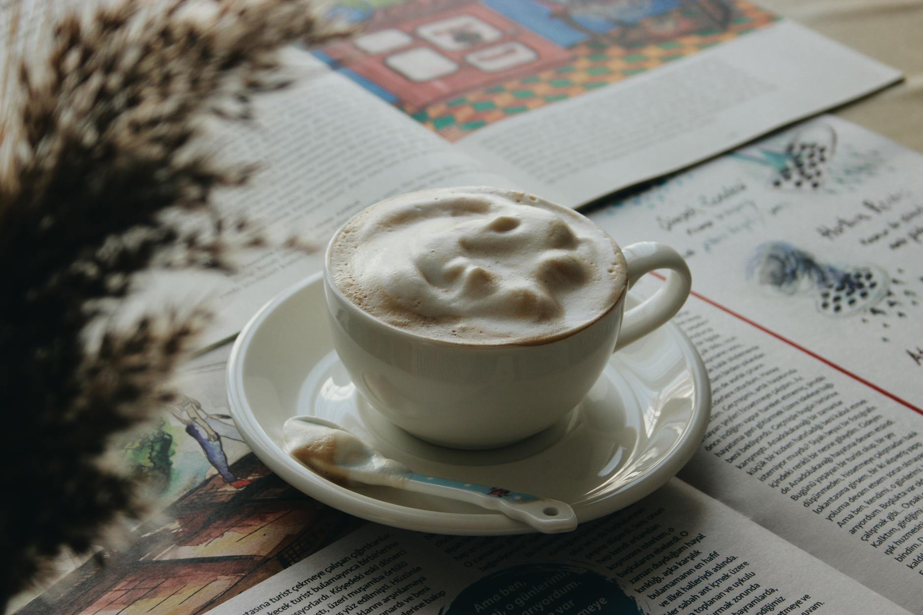 Filiżanka kremowego cappuccino na spodku obok porannej lektury