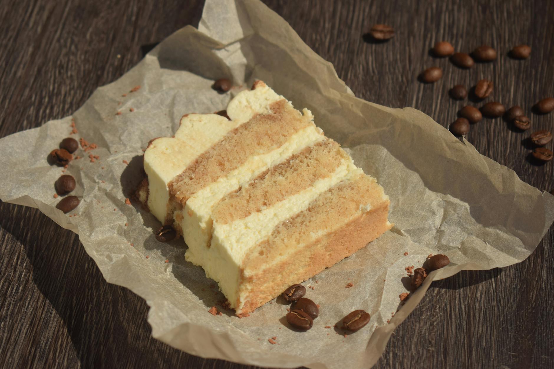 Kawałek tiramisu na pergaminie otoczony ziarnami kawy