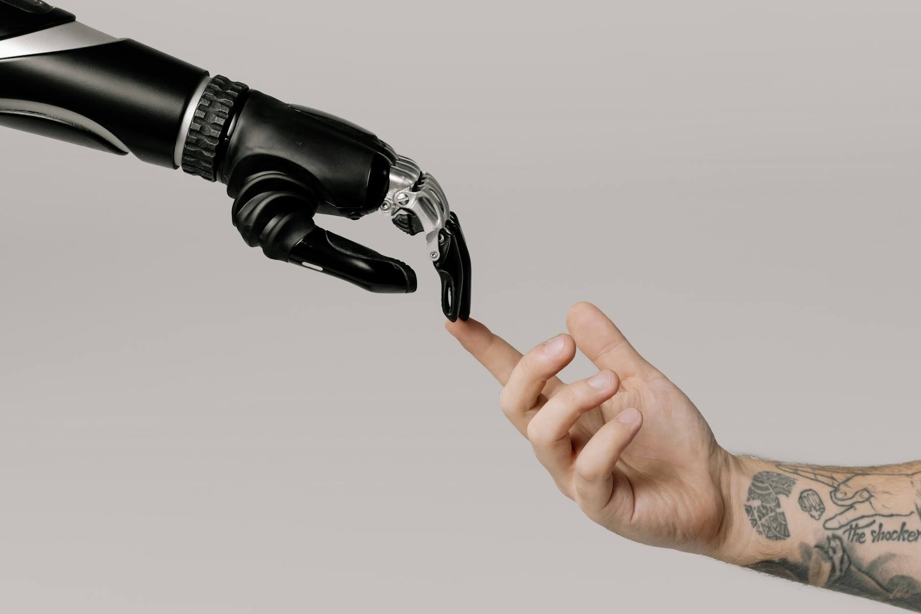 Ludzka wytatuowana dłoń sięga do mechanicznej dłoni robota