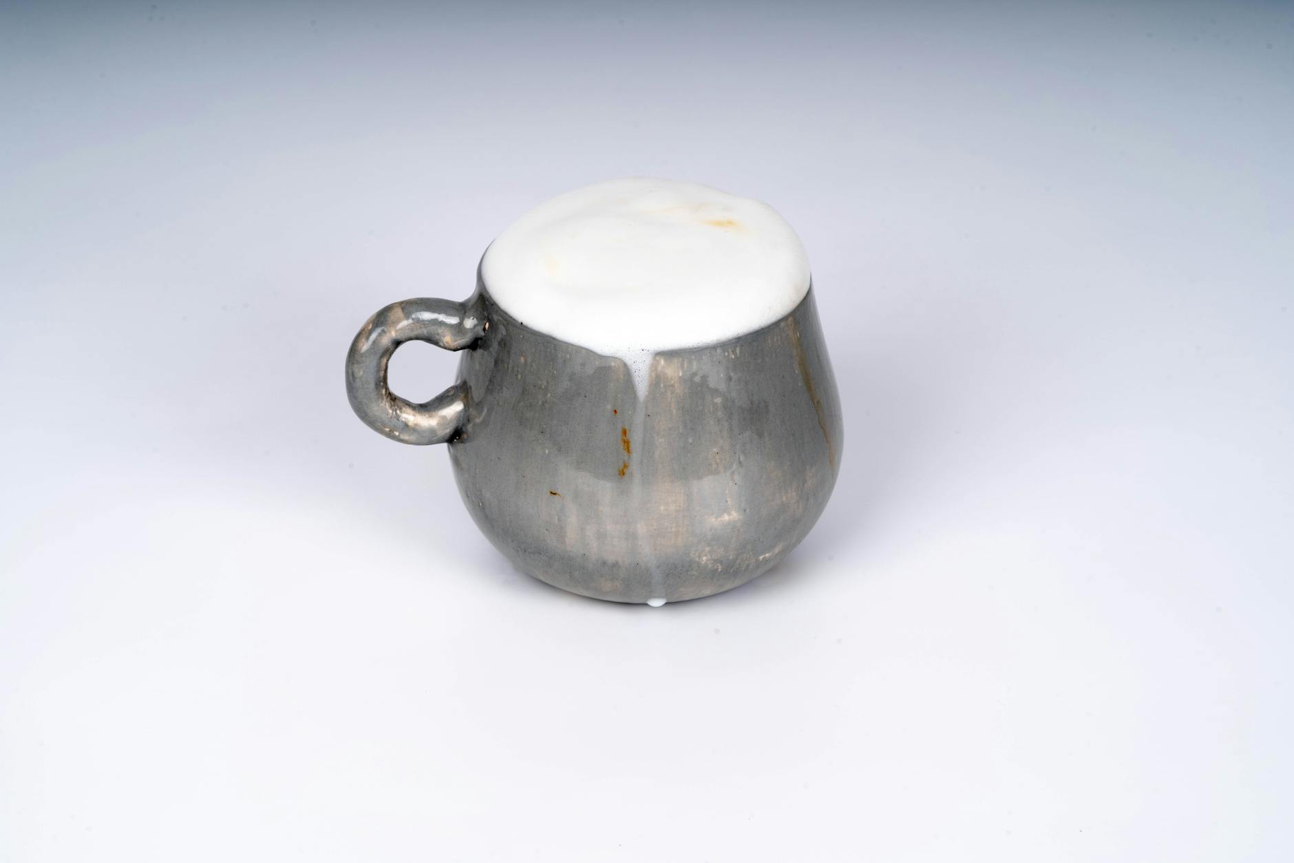 Metaliczny kubek z kremową pianką cappuccino na białym tle
