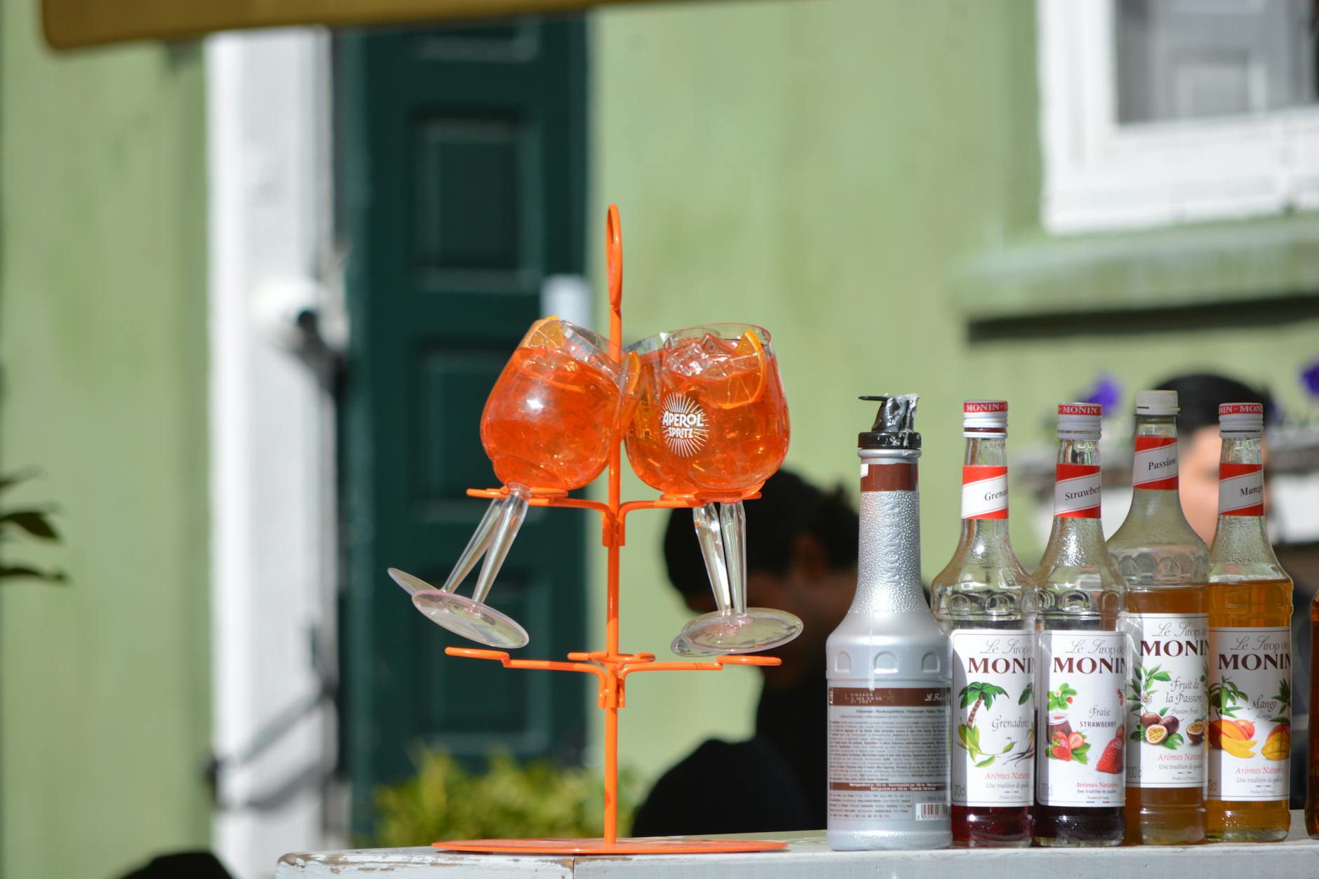 Szklanki Aperol Spritz i syropy Monin na letnim stole na zewnątrz
