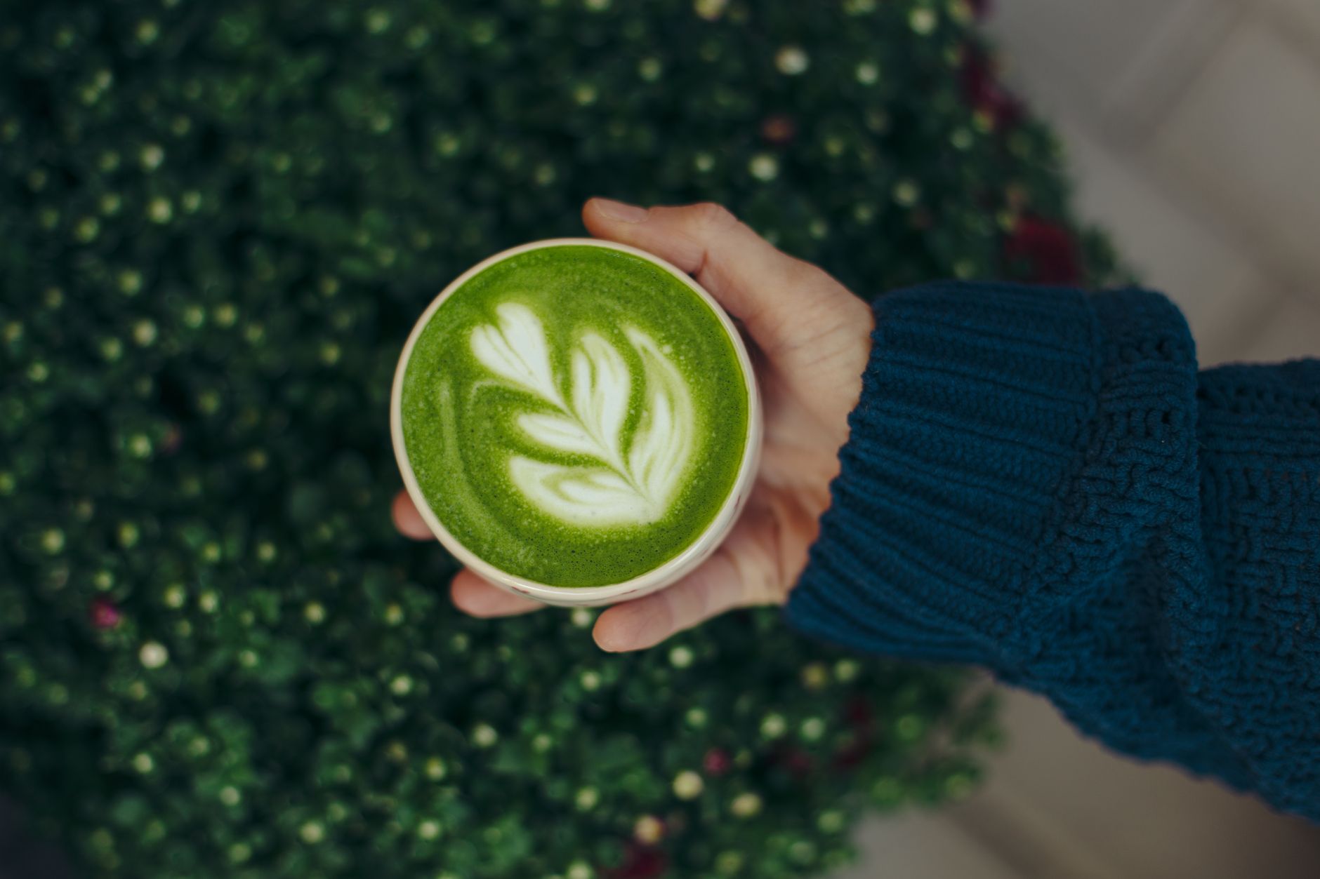 Dłoń w swetrze trzyma filiżankę zielonej matcha latte z latte art