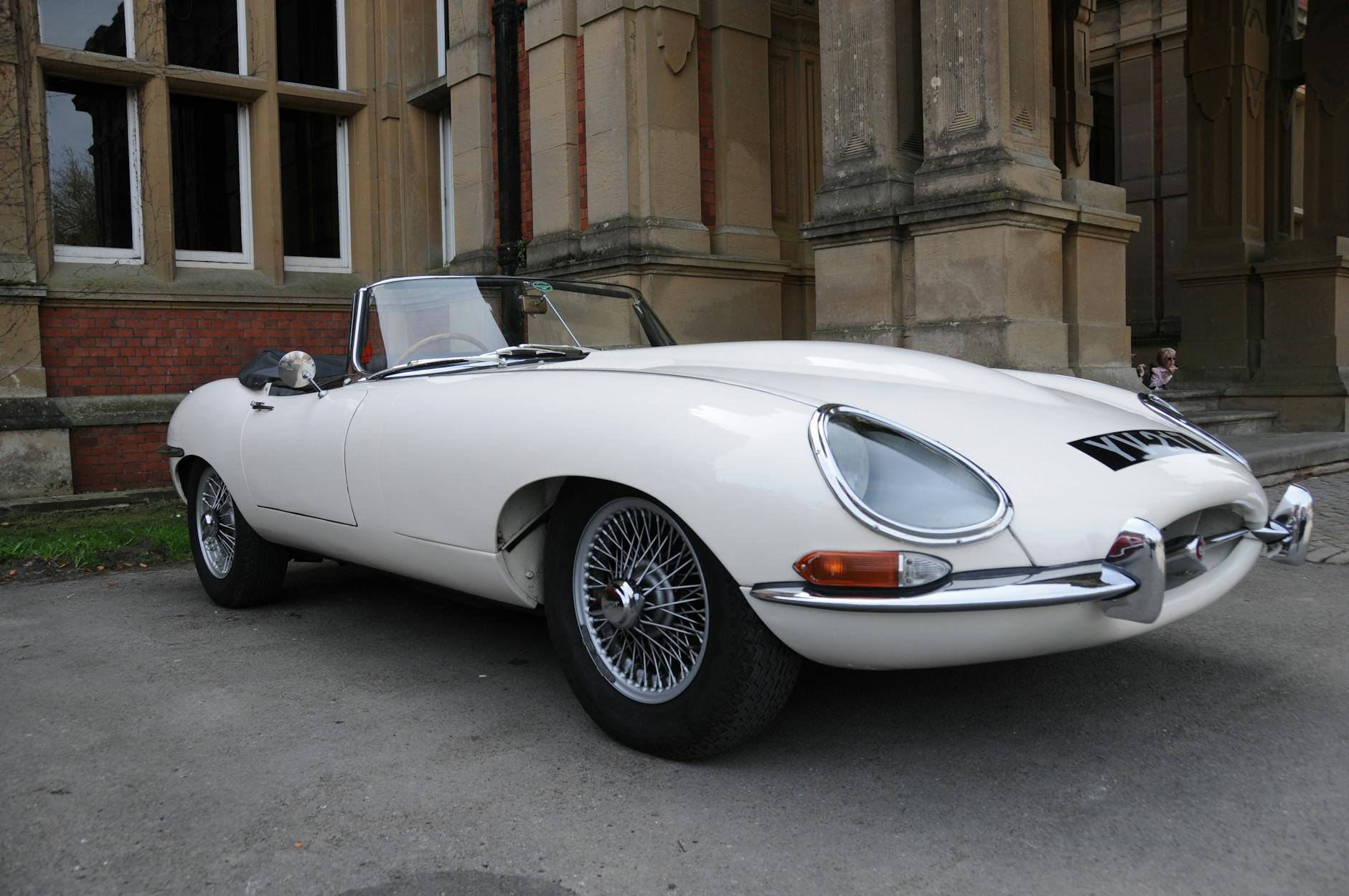 Klasyczny biały Jaguar E-Type zaparkowany przed zabytkowym budynkiem