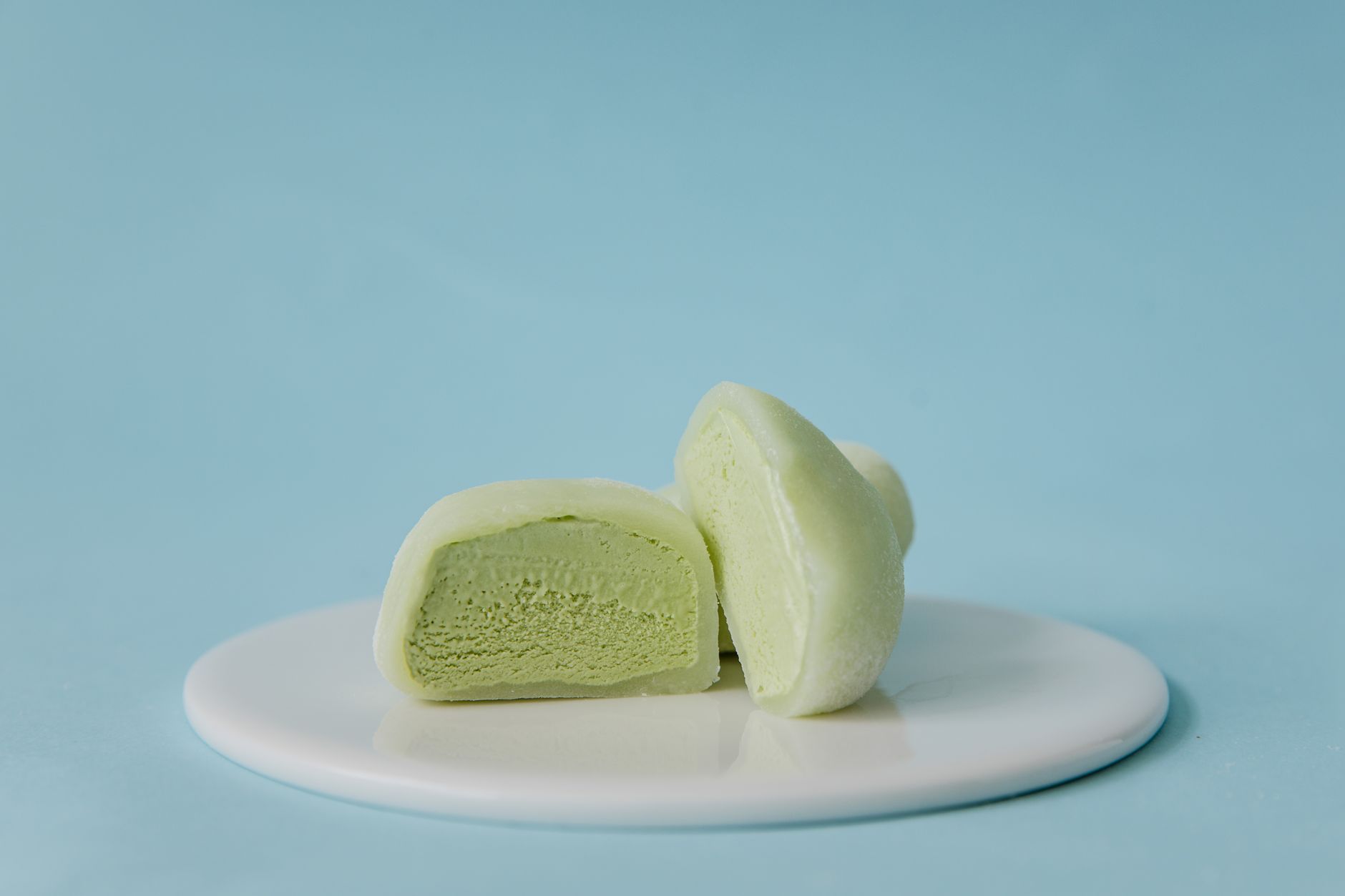 Zielone mochi z herbatą matcha na białym talerzu na pastelowym tle