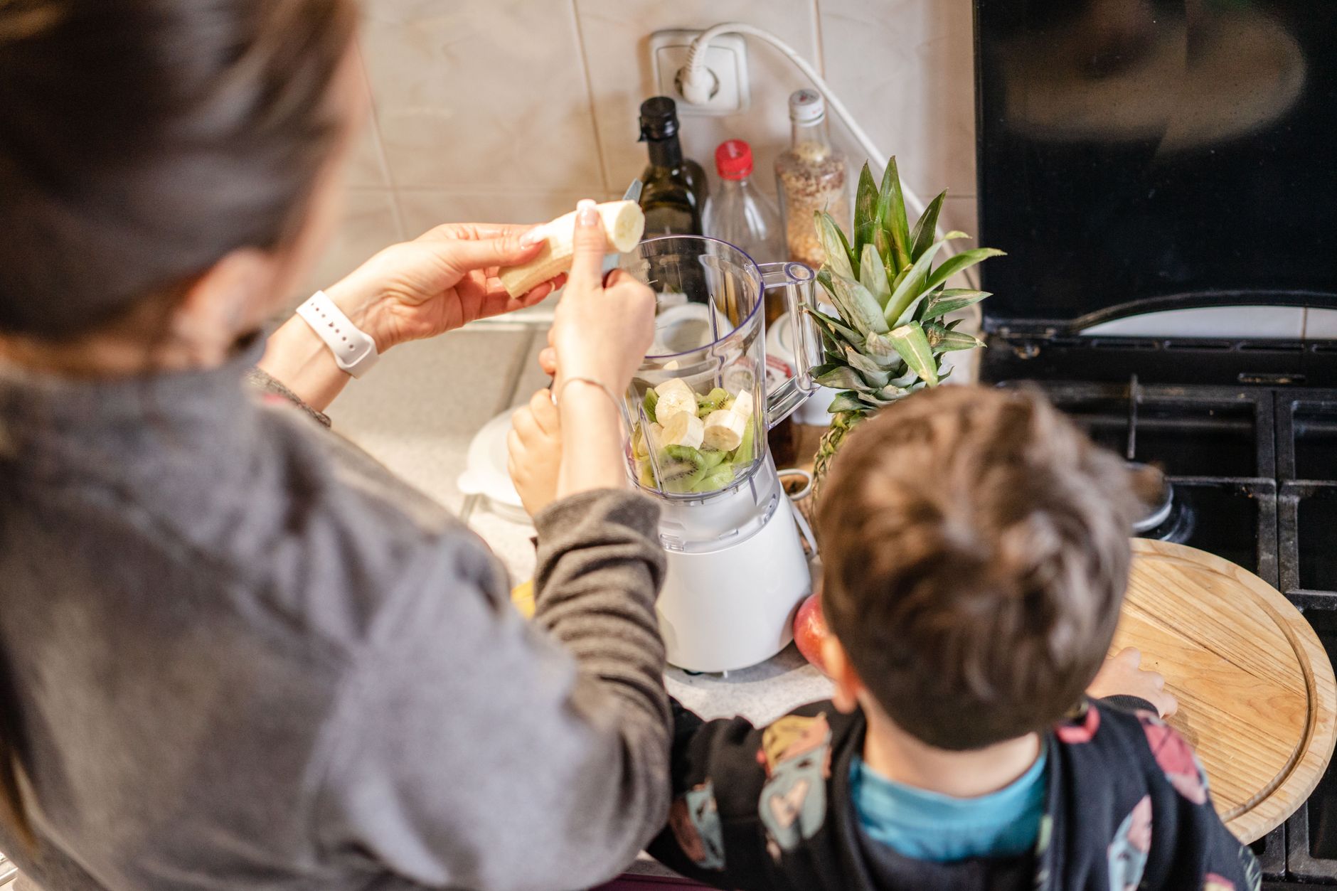 Mama z dzieckiem blendują banany i ananasa na smoothie w kuchni